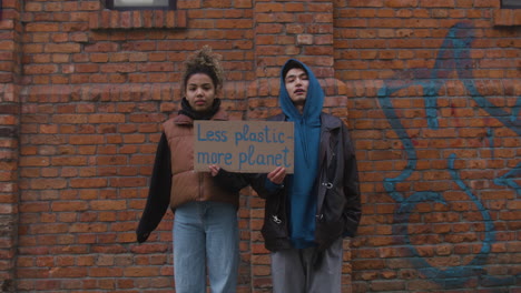 young male and american female activists looking at camera and holding a cardboard placards during a climate change protest