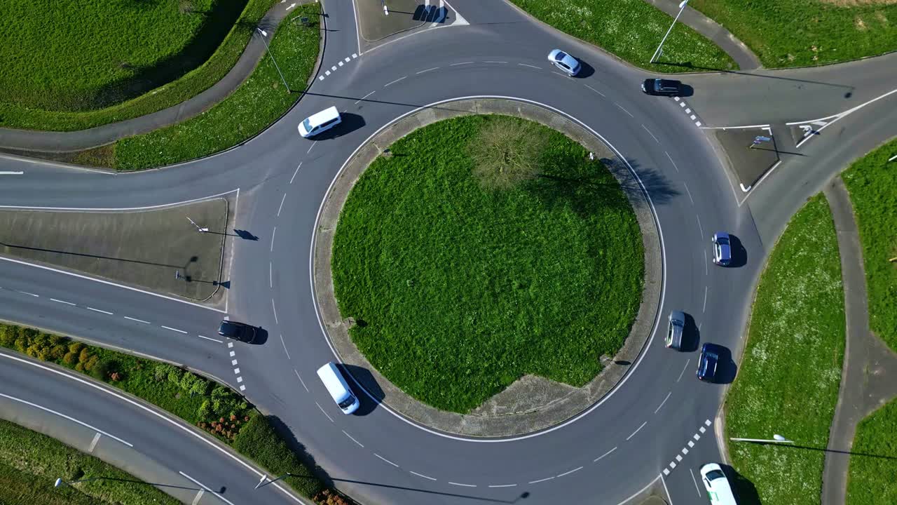 Busy traffic roundabout with green center, transportation infrastructure and traffic flow. Aerial top-down view