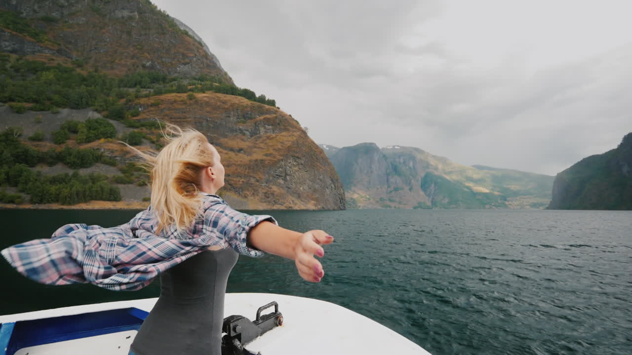 una mujer libre se para con las manos a los lados en la proa de un crucero que viaja por los fiordos de