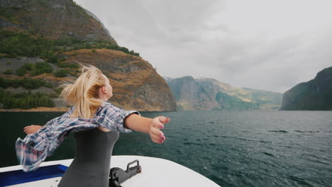 Eine-Freie-Frau-Steht-Mit-Den-Händen-An-Den-Seiten-Am-Bug-Eines-Kreuzfahrtschiffes,-Das-Durch-Die-Fjorde-Fährt