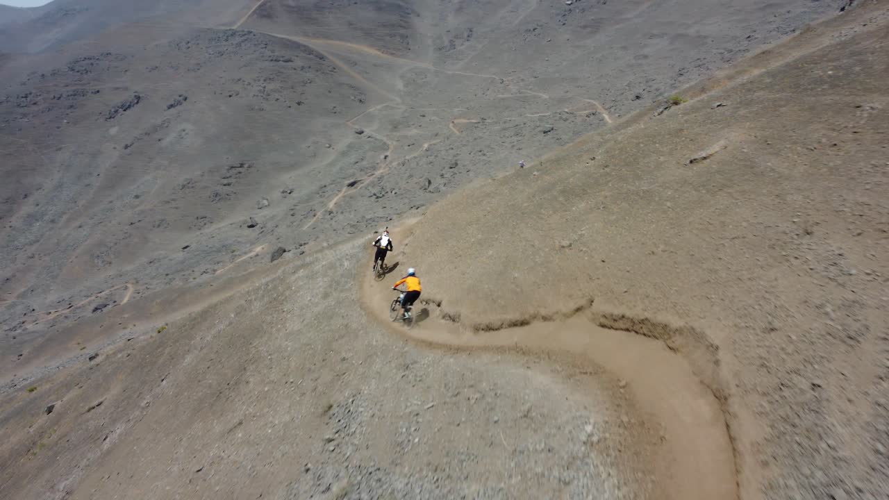 두 명의 산악 자전거 타는 사람을 따라 바위 언덕을 따라 내려가는 역동적인 드론 샷