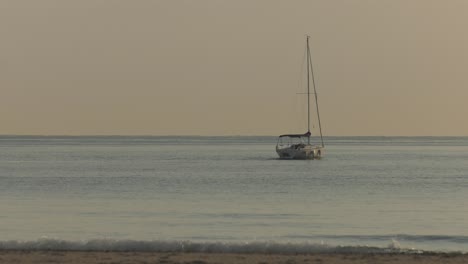 calm dawn sea with sailing yacht heading to horizon, sails furled