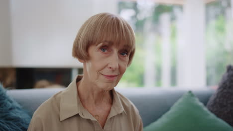 senior woman posing at camera. closeup positive woman sitting on sofa in room