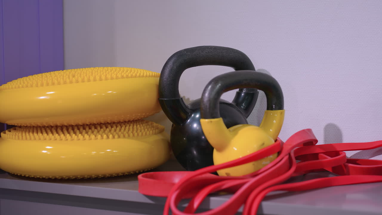 Close-up of various gym equipment, including kettlebells, resistance bands, and balance discs, neatly arranged on a shelf, creating an organized and functional workout space