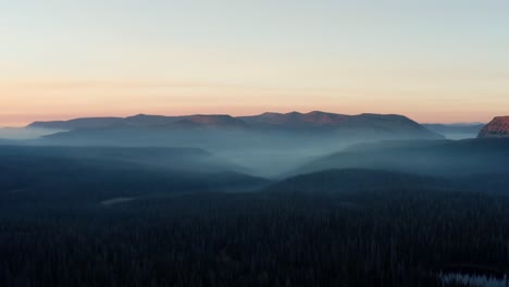beautiful left trucking aerial drone shot of the stunning wild uinta wasatch cache national forest in utah with large pine trees below and stunning mountains covered in mist during a summer sunrise