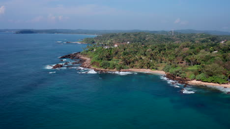 drone orbital shot around a scenic tropical headland with palm trees, rocky shorelines, and turquoise water near silent beach, sri lanka during midday.