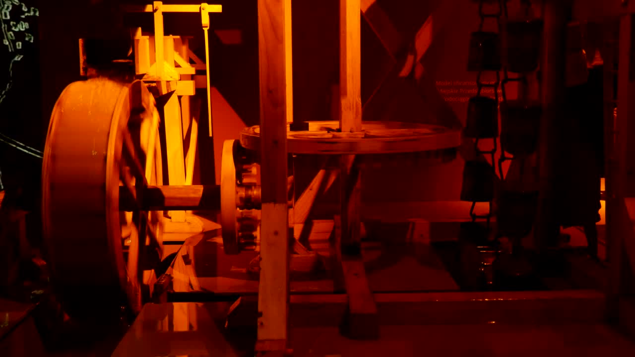 Arty view of a traditional yellow water mill model with a spinning wooden wheel with blades, falling water stream, a set of cogs and poles
