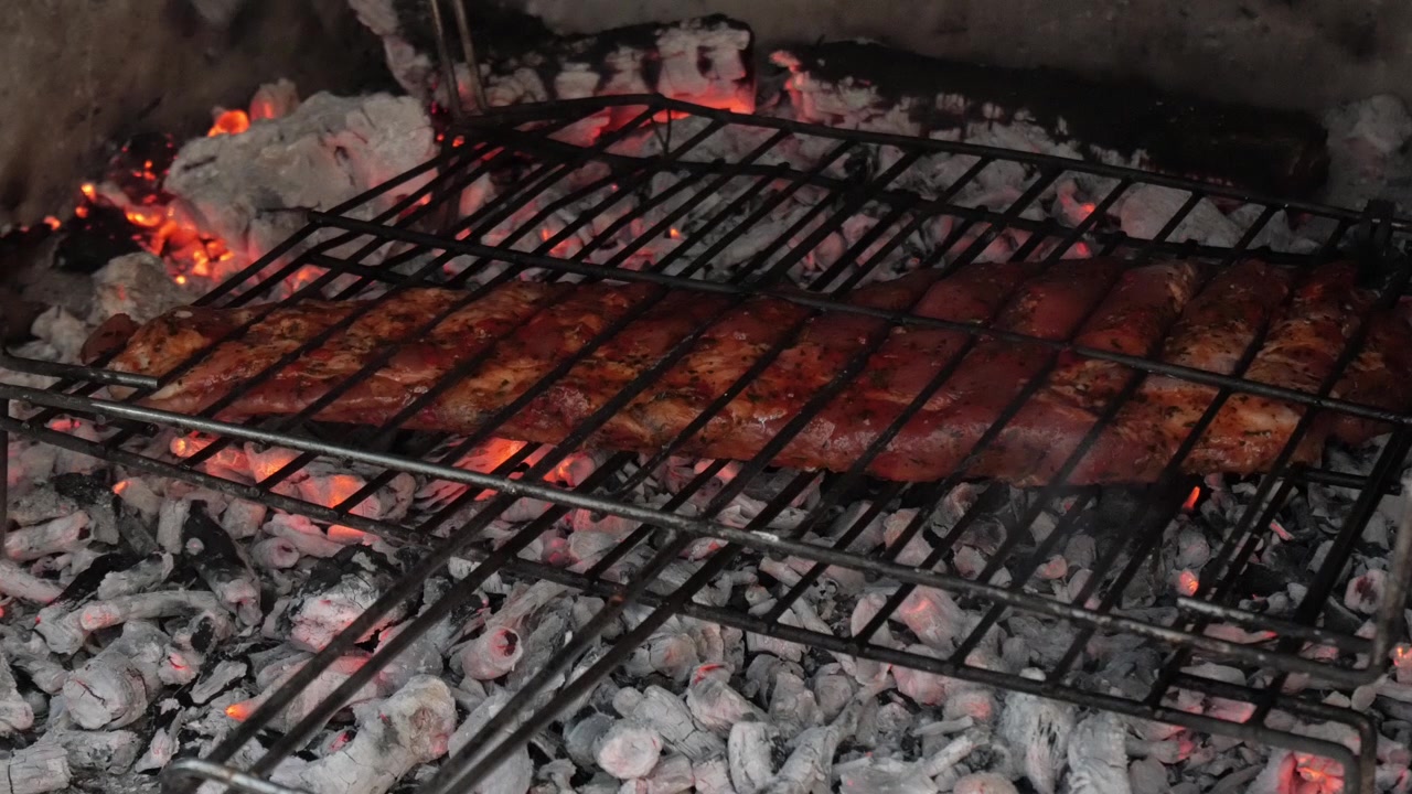 Salsicce che grigliano su carboni ardenti, fiamme visibili in un allestimento barbecue rustico
