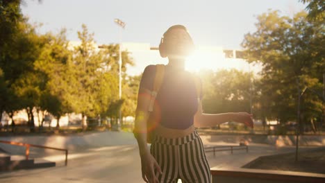 portrait of a girl with a short haircut in a purple top, striped pants and red headphones is dancing on roller skates in a skatepark at sunset in summer