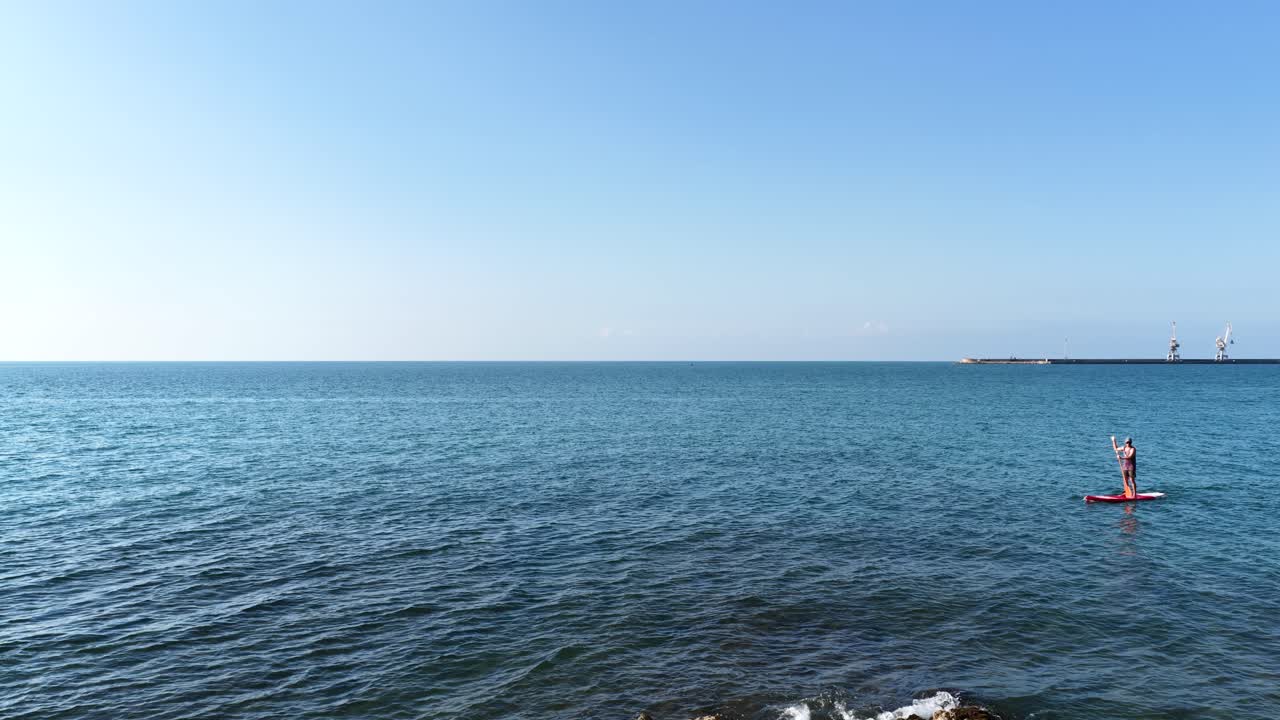 Athlete paddle boarding in calm ocean waters near breakwater