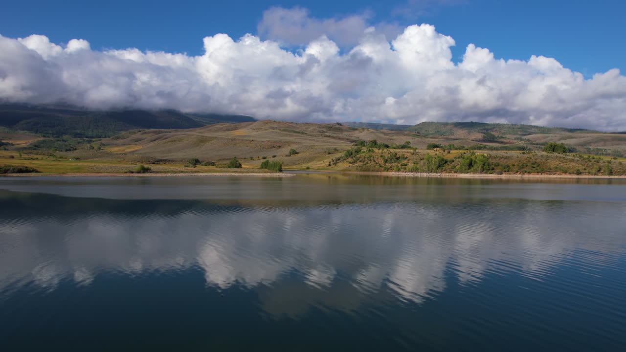 tomado por un dron, un lago azul prístino y colinas verdes bajo nubes esponjosas en un soleado día de primavera.