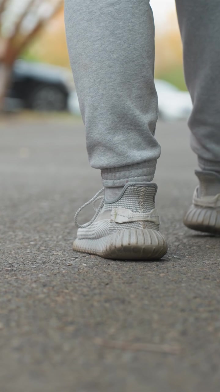 Individual dressed in casual attire progressing forward. Subject stride highlighted by visible tread patterns. Background shows hints of trees structures on paved outdoor