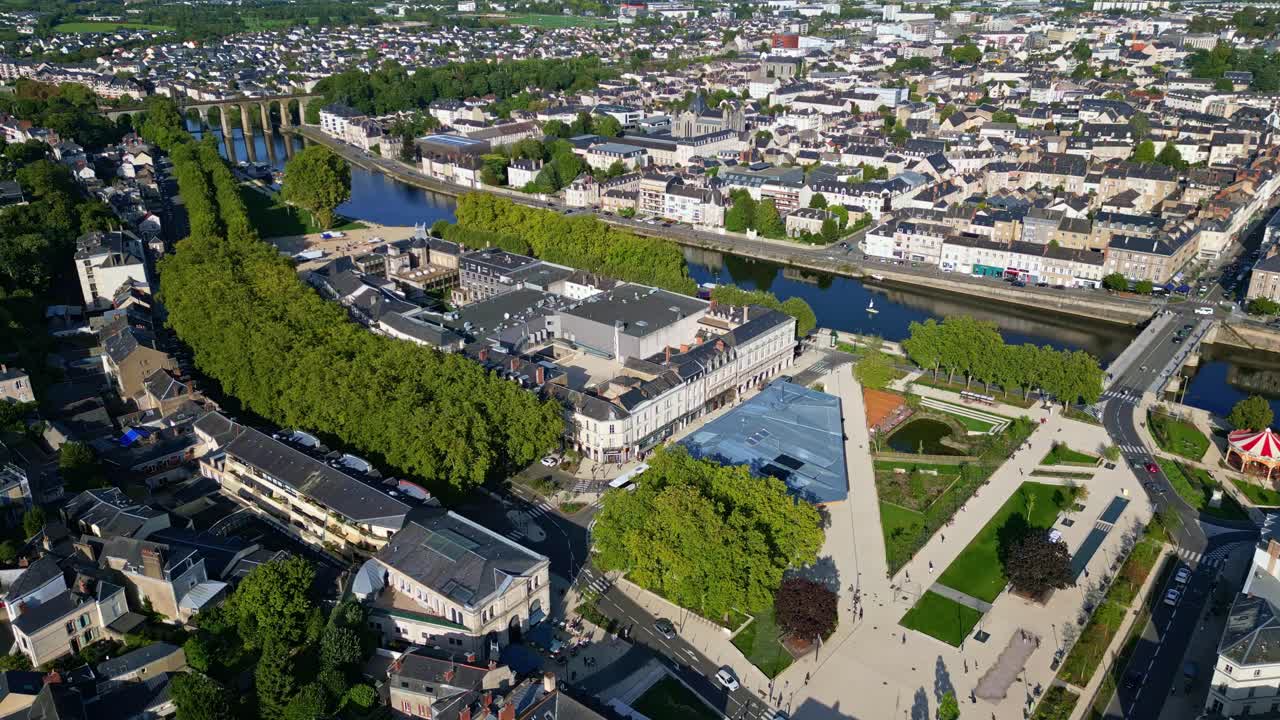 Drone establishing shot glides over renovated Place du 11 Novembre in Laval, France, revealing new open city square, the Halles de Laval market and event building and tree-bordered Mayenne riverbank