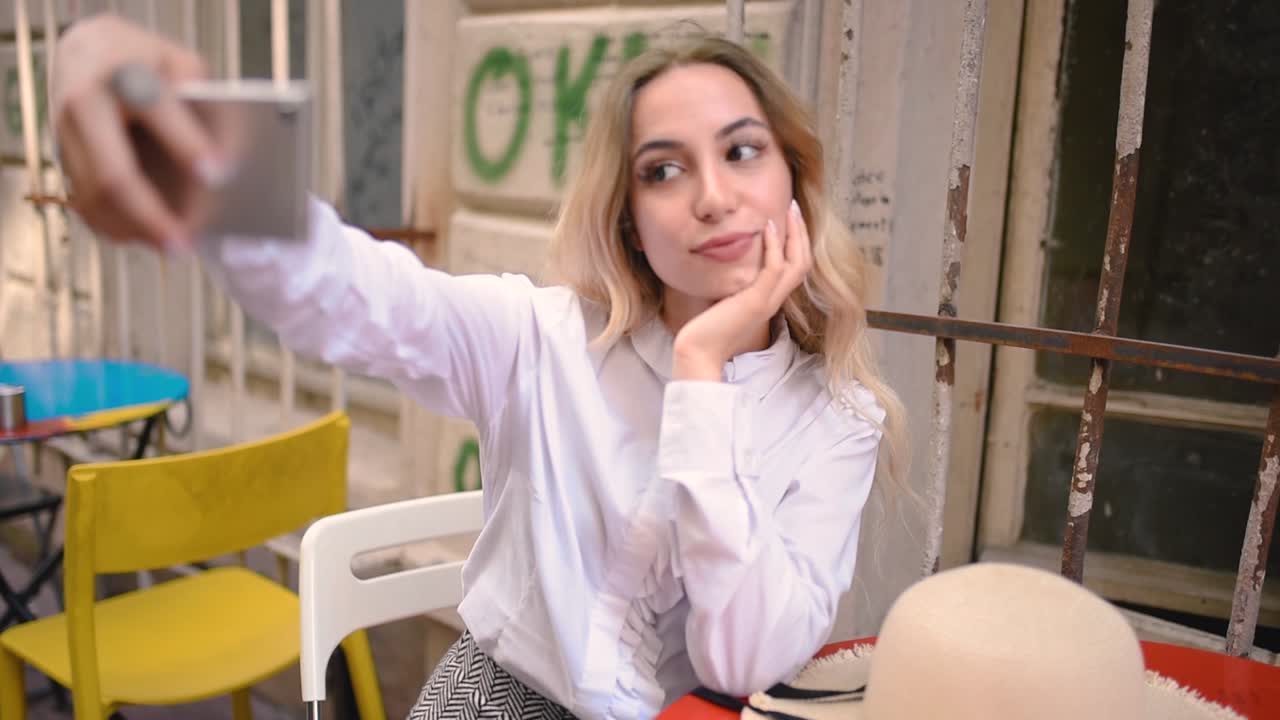 atractiva joven hermosa se toma selfie mientras se sienta en un café afuera