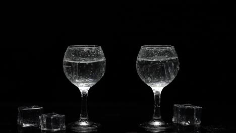 two glasses of water with ice on a black background