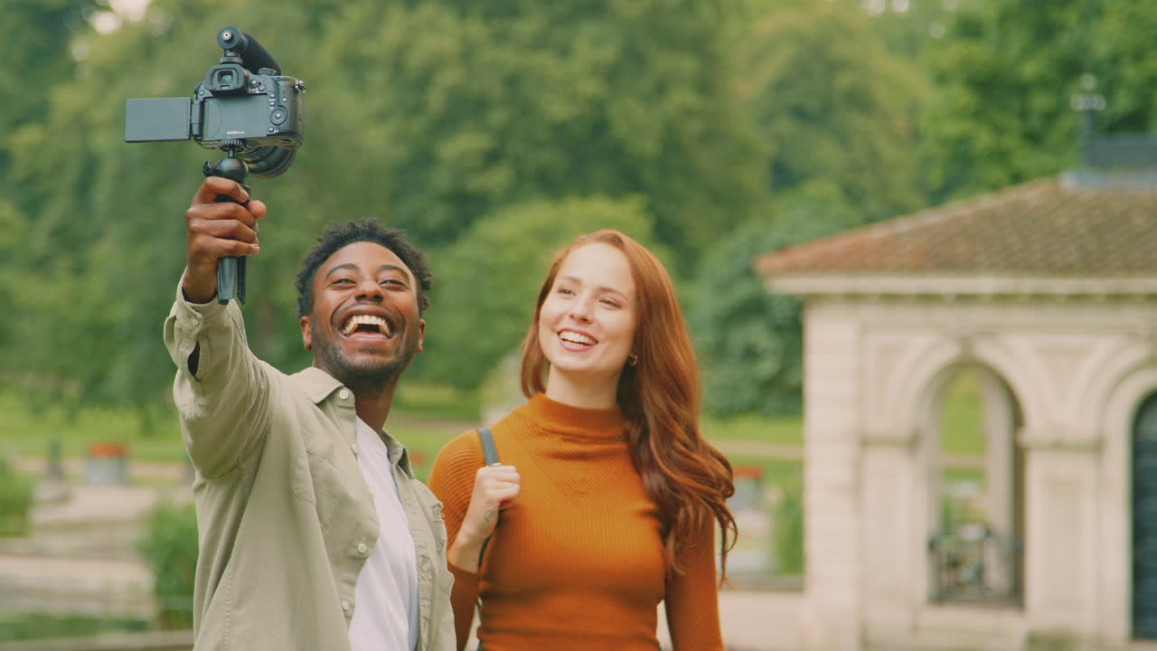 젊은 부부 가 함께 도시 를 여행 하고 공원 에 있는 비디오 카메라 에 블로그 를 하고 있다