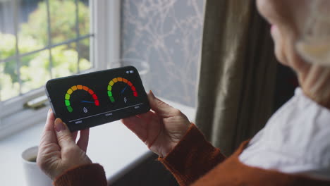 senior woman with smart meter trying to keep warm by radiator during cost of living energy crisis