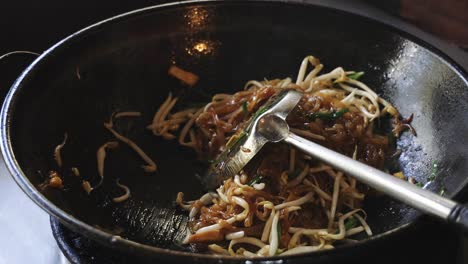 cooking pad thai series: chef stir-frying pad thai noodles with prawns in smoking hot wok at thai street food shop