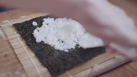 older woman hands putting rice on sushi seaweed wrapping in kitchen