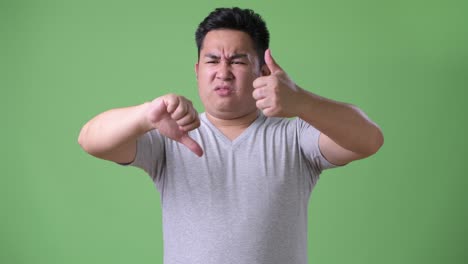 young handsome overweight asian man against green background