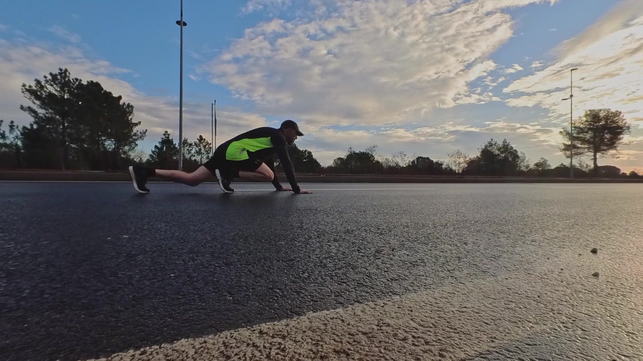 Low angle shot of a runner starting a sprint from a crouch position on an empty asphalt road. Dramatic morning sky. Concept of explosive power, goals, and motivation.