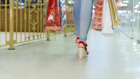 young woman in jeans and red shoes walking on the mall rear view the frame can be seen only the legs