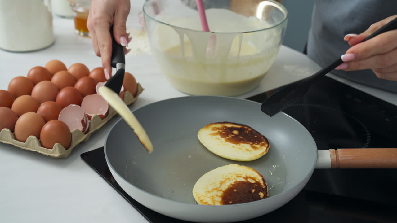 Woman flipping pancakes next to egg cup. Slow motion close up