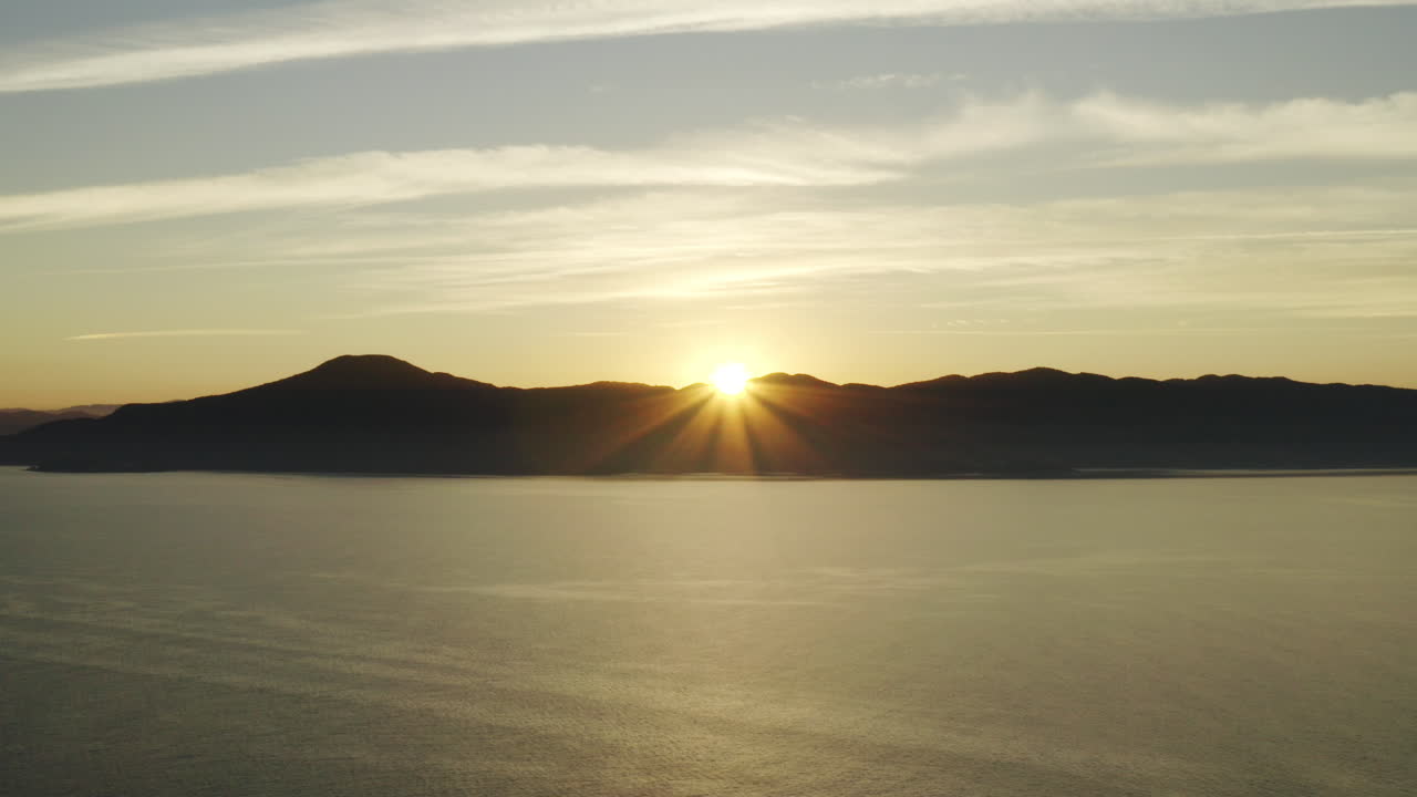 Beautiful aerial drone view sunset going down over the ocean and mountains on the horizon