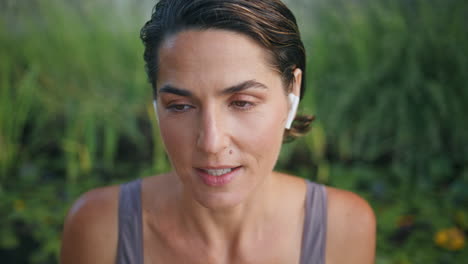 auriculares de primer plano mujer deportista hablando en el parque verde. mujer cara llamando en línea