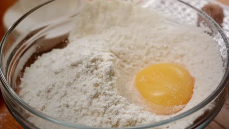 macro shot of a kitchen whisk breaking a yellow egg in flour in ultra slow motion