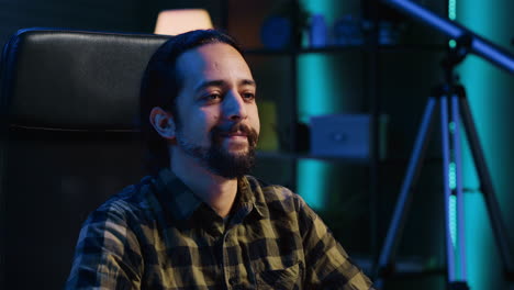 hombre sonriente sentado en una silla en el escritorio de la oficina de casa en un apartamento iluminado con neón