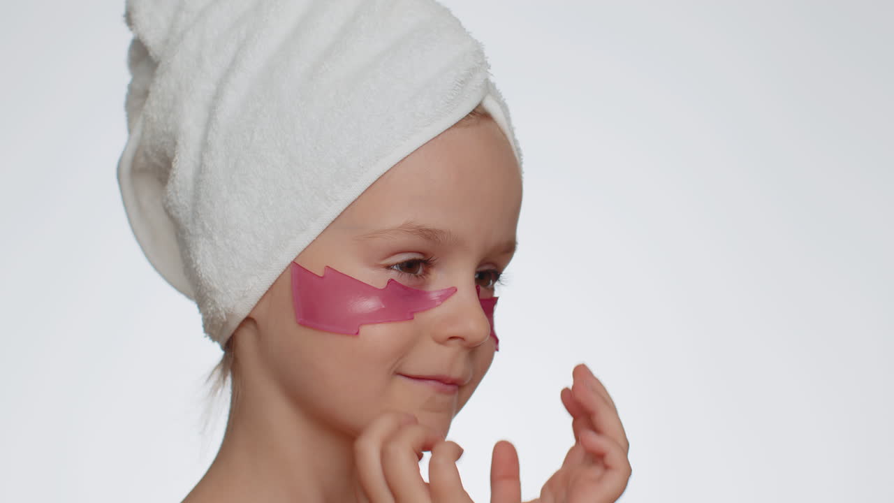 Smiling child girl applying pink patches under eyes, teenager natural skin care, perfect fresh clean