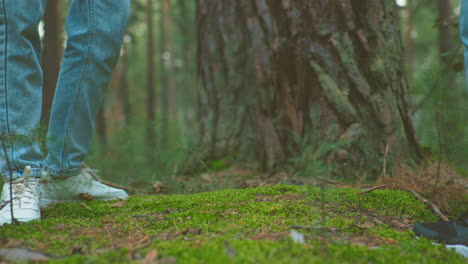 close-up of women in jeans and sneakers zipping up backpacks retrieved from forest ground, surrounded by tall trees and lush greenery, they lift their bags and walk forward