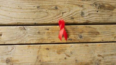 Video-of-close-up-of-red-cancer-ribbon-on-wooden-background