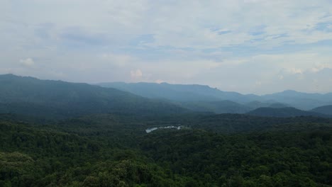 Eine-Umgekehrte-Luftaufnahme-Eines-üppigen-Regenwaldes-Und-Berge-Am-Horizont,-Ein-See-In-Der-Mitte,-Der-Wie-Ein-Juwel-Aussieht,-Ein-Herrlicher-Himmel-Am-Nachmittag