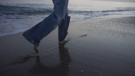 girl running barefoot in long jeans along the shore of the beach during sunset