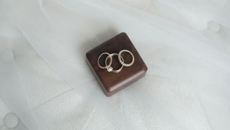 evoke the romance of a wedding day with a close-up of engagement and wedding rings resting on a handcrafted wooden box, atop a plush white pillow, symbolizing lasting love and commitment.