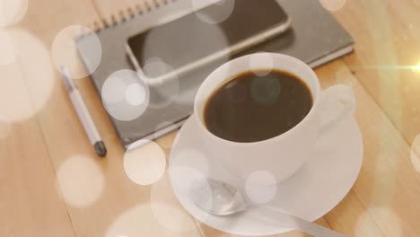 Animation-Von-Weißen-Lichtpunkten-über-Einer-Tasse-Kaffee-Und-Einem-Smartphone-Auf-Dem-Schreibtisch