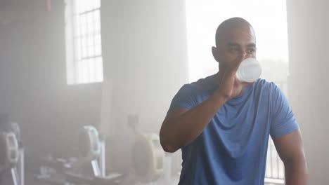 tired biracial man resting and drinking water after training at gym, in slow motion