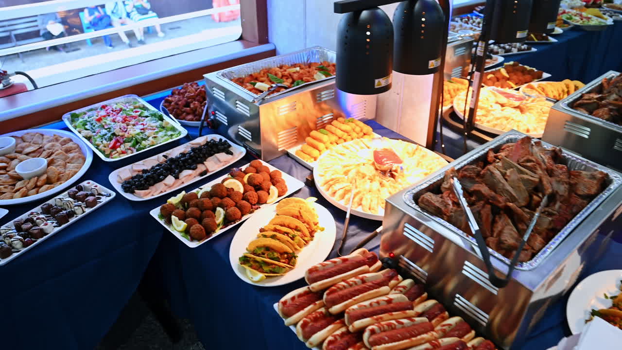 New York, USA, 1 agosto 2025: tavolo da buffet con un'ampia varietà di piatti caldi e freddi su una nave da crociera. Grande buffet allestito su una nave da crociera con maccheroni, hot dog, tacos, snack fritti, frutta e insalate sotto luci calde
