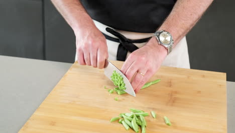 male chef chop the green bean with his knife on the cutting board at his kitchen