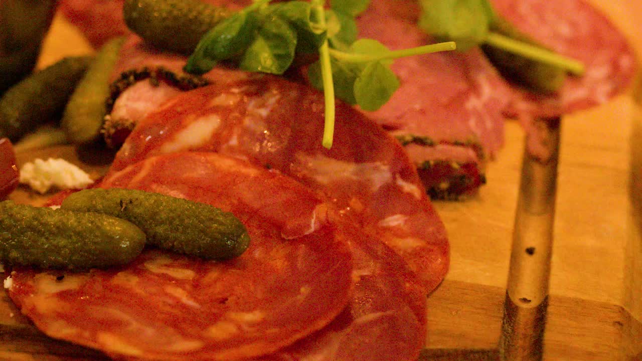Close-up of fork lifting salami from charcuterie board with cheese, pickles, and garnish