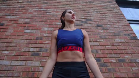 fit young brunette woman with a sport outfit lifting a dumbbell exercise outdoor in front of a brick wall