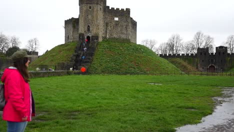 Rainy-day-at-Cardiff-Castle-with-a-woman-looking-at-tourists-climbing-Norman-Fortress-mound,-Wales