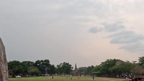wide view of a park with lush trees and a cloudy sky, framed by a stone structure.