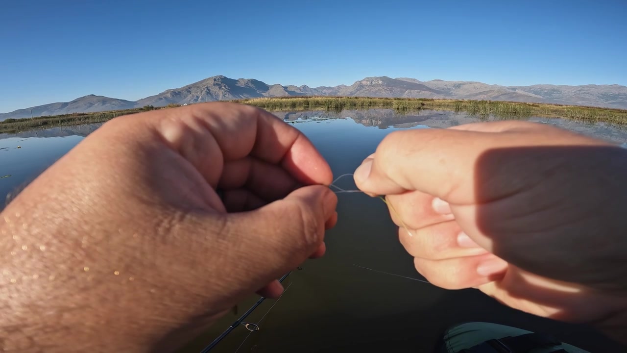 Pescatore lega esca artificiale, amo su lenza in monofilamento, POV lago di montagna