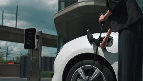 progressive businesswoman plugs charger plug from charging station to his ev.