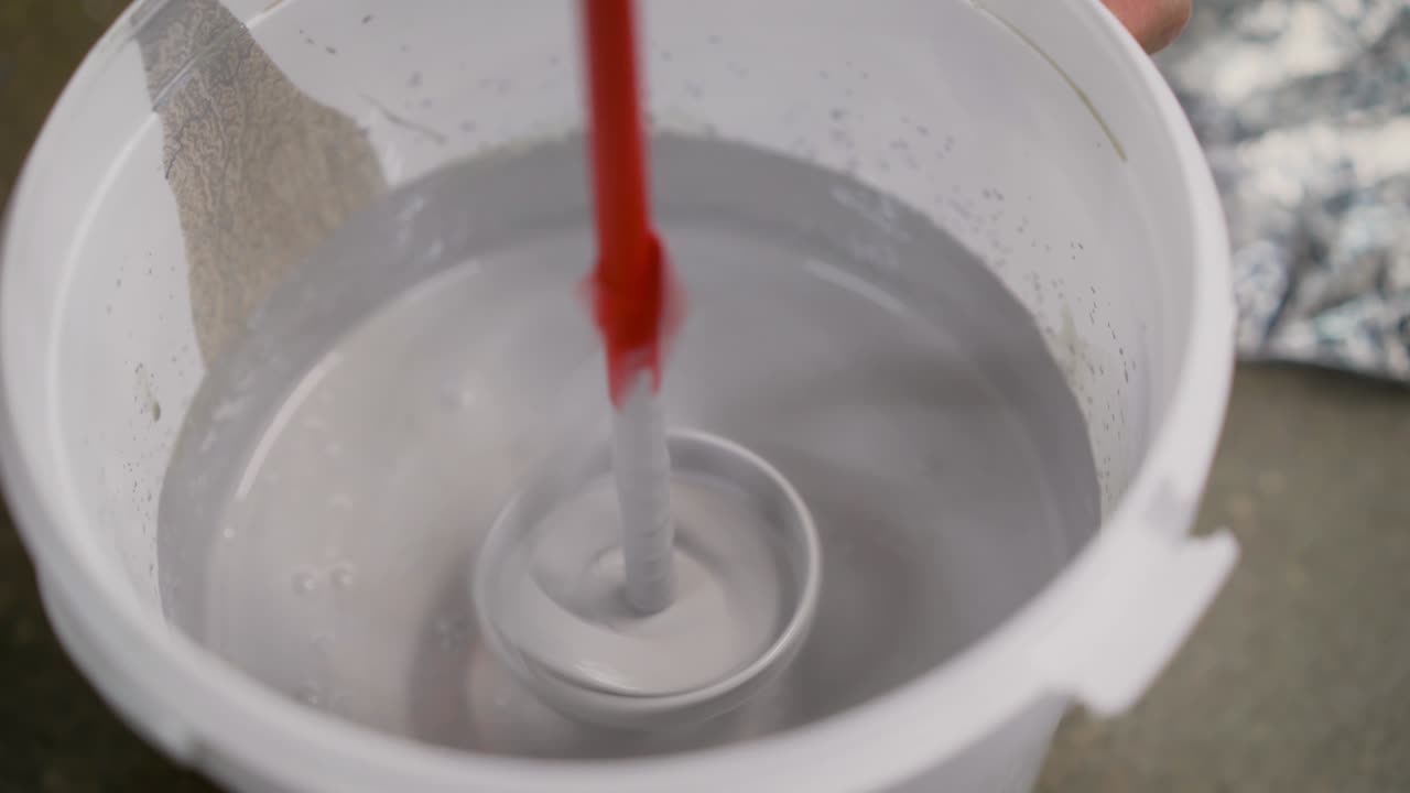 Drill paddle mixer on a bucket with white paint, DIY tools and accessory, banner. The white paint is mixed in a bucket with a drill