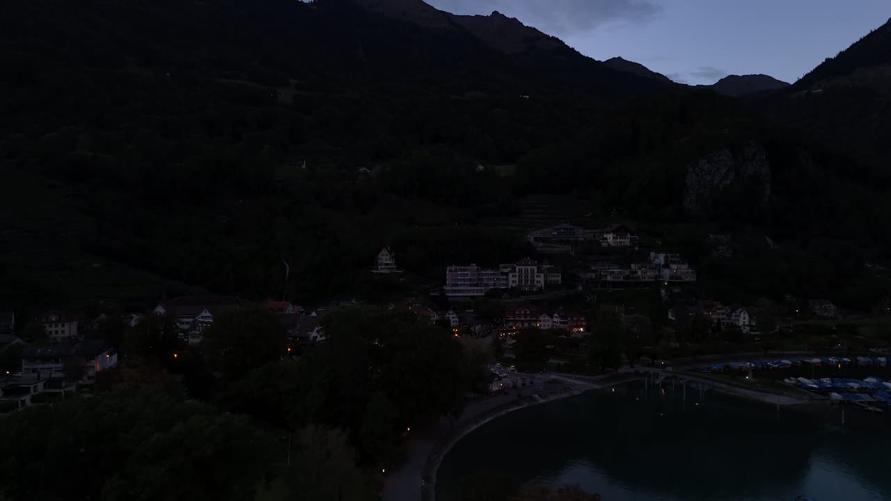Aerial view of a residential area showcasing the calm waters of Lake Walensee in Switzerland during late evening, with dusk softly descending, creating a serene and picturesque atmosphere.