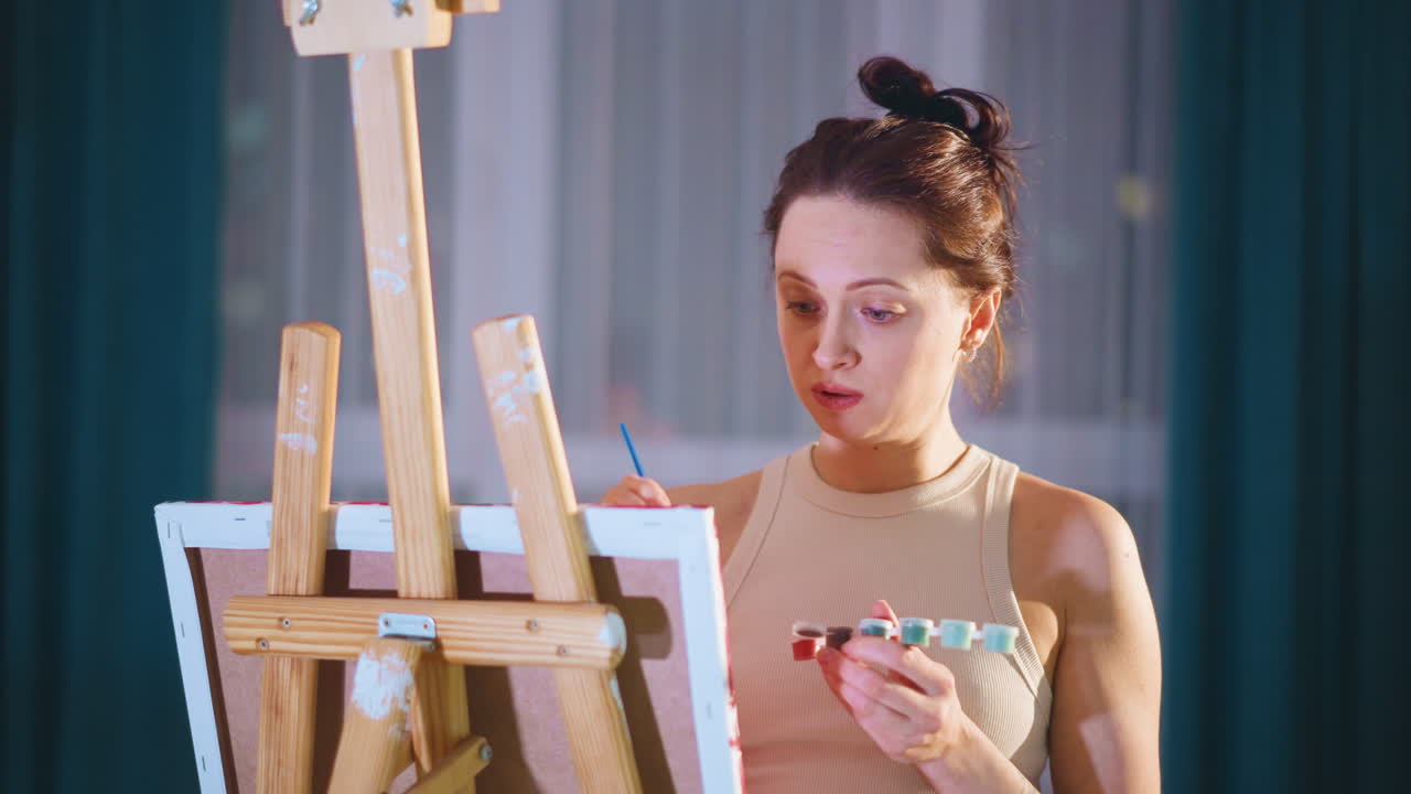 Artist Chooses Colors, Artist Attentively Evaluating Color Choices In Her Personal Art Studio, Caucasian Female Artist Carefully Assessing And Choosing Colors At Her Easel In Evening Studio